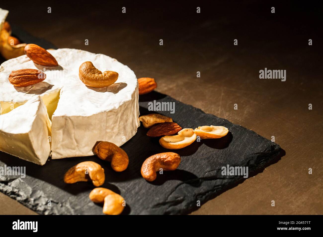 Different kinds of nuts lie on brie cheese on black dish Stock Photo
