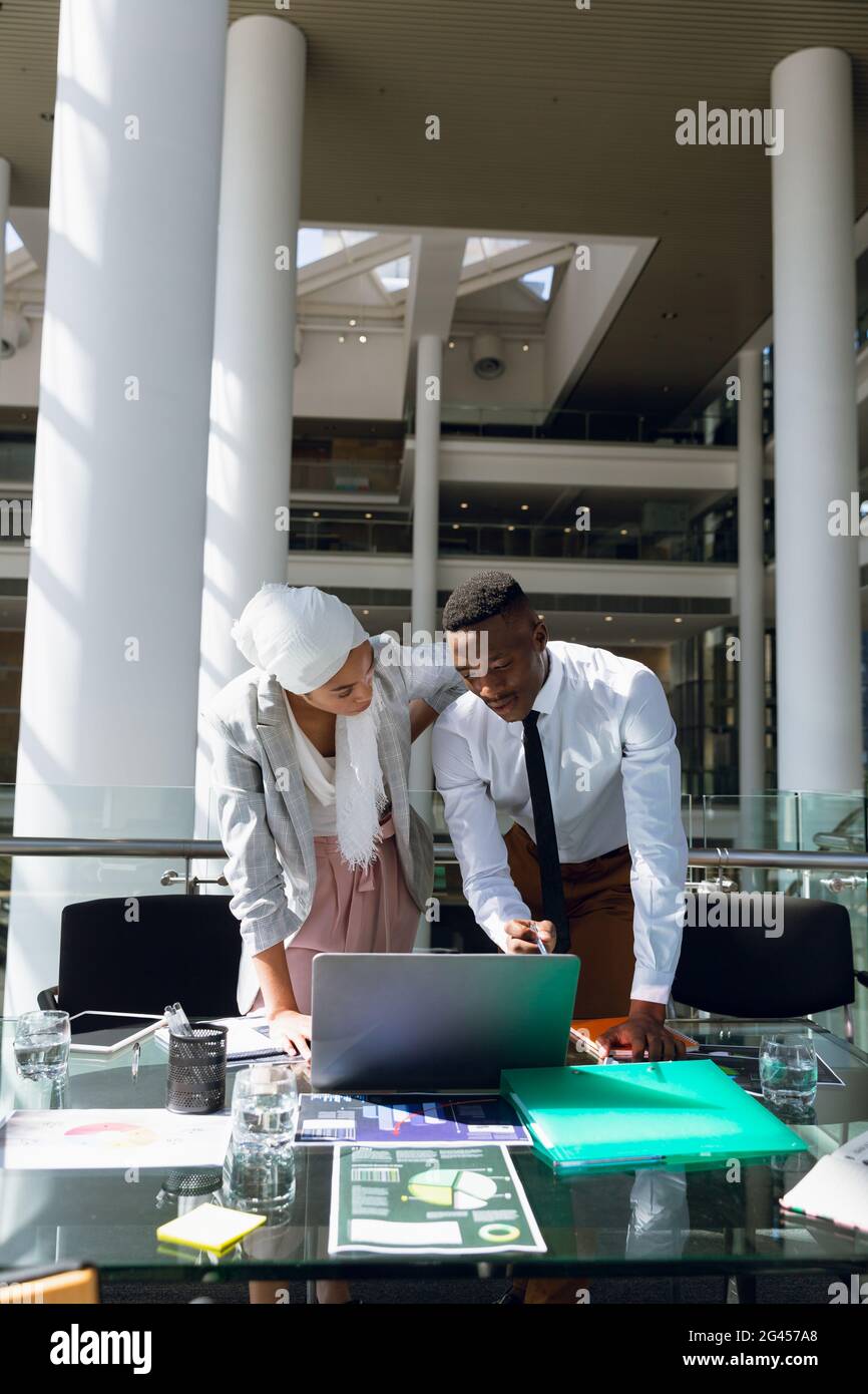 Male and female executives discussing over laptop at desk Stock Photo