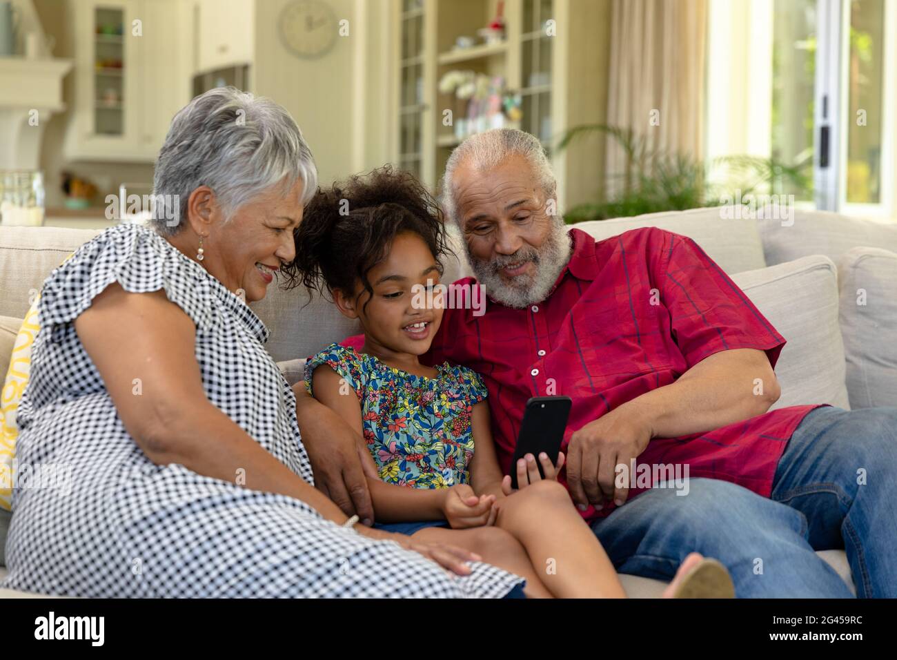 Senior mixed race couple sitting on the couch with their young  granddaughter Stock Photo