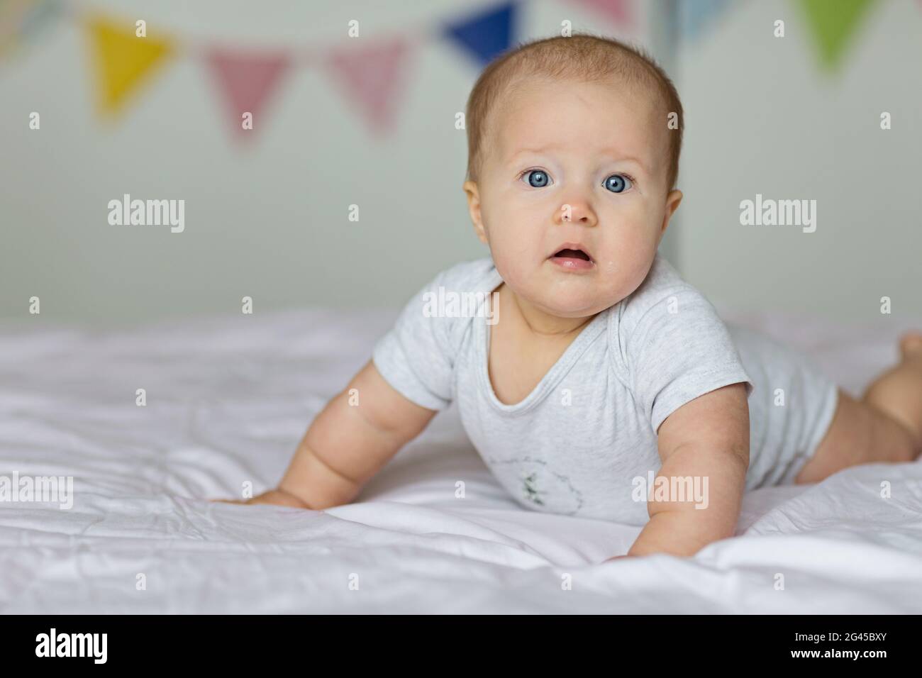 Caucasian blonde baby six months old lying on bed at home. Kid wearing