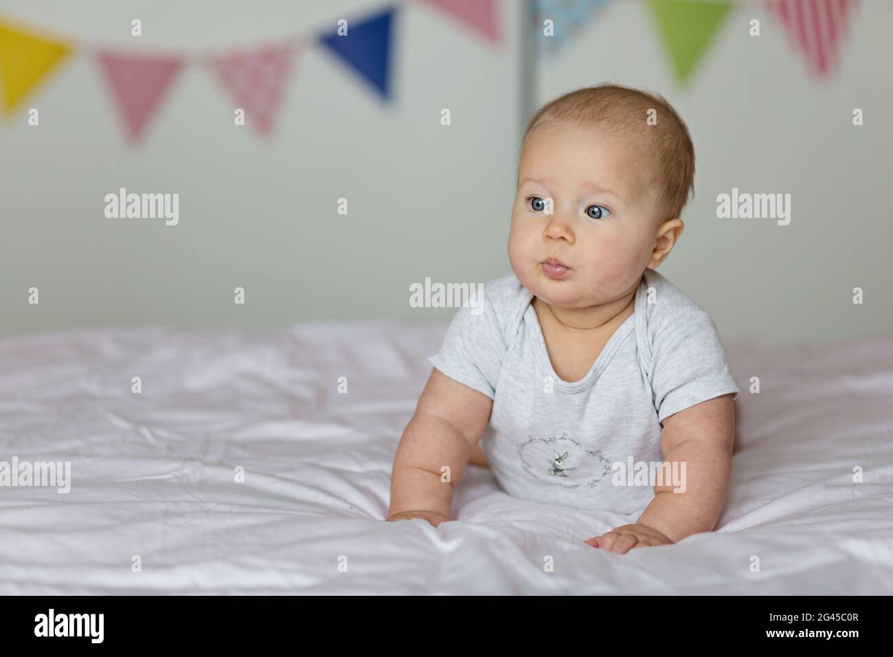 Caucasian blonde baby six months old lying on bed at home. Kid wearing cute gray clothing