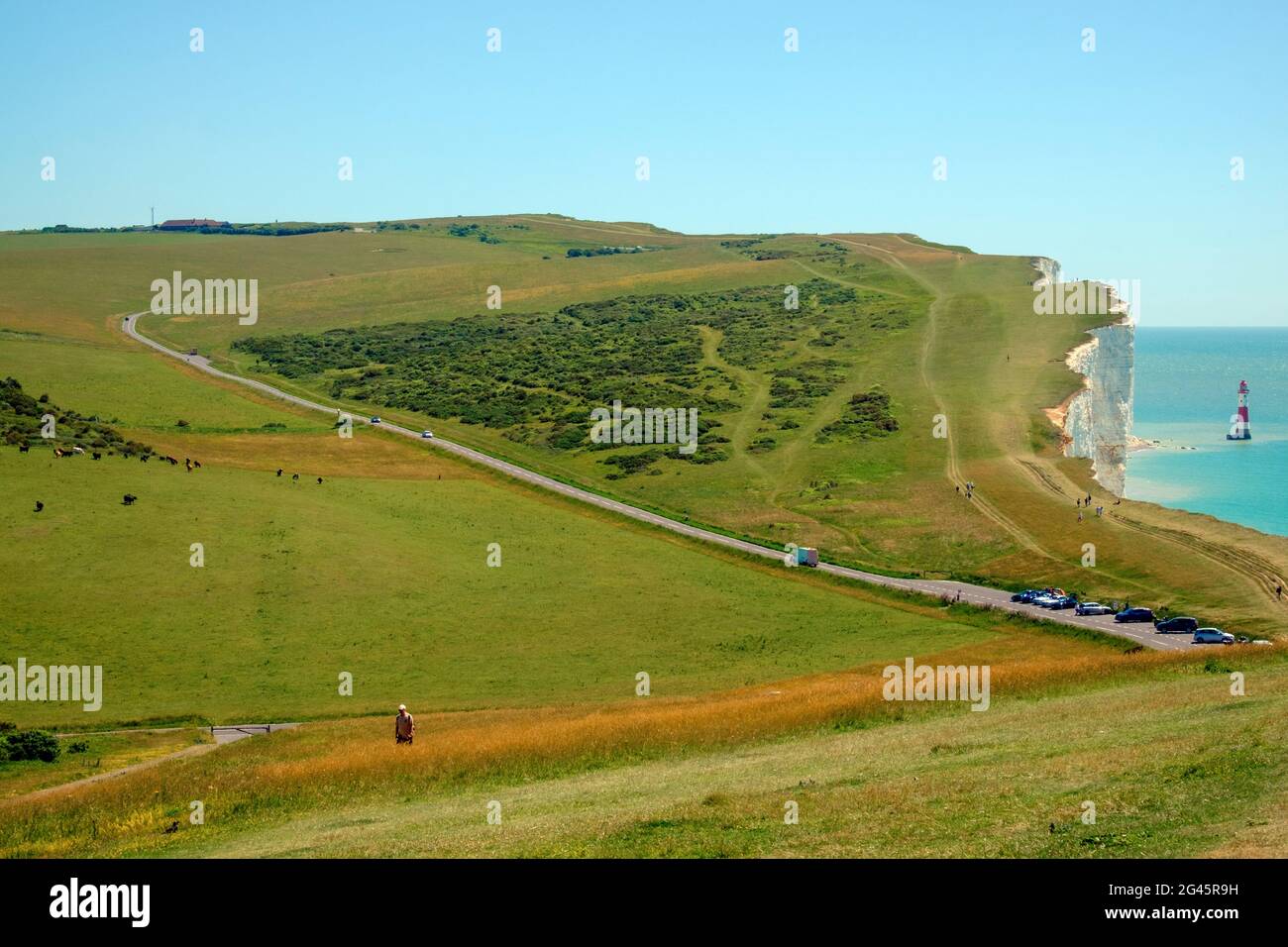 Staycation idea. Beachy Head Lighthouse in the English Channel with white chalk cliffs, Beachy Head Rd, Parked cars, grassland & tourists. East Sussex Stock Photo