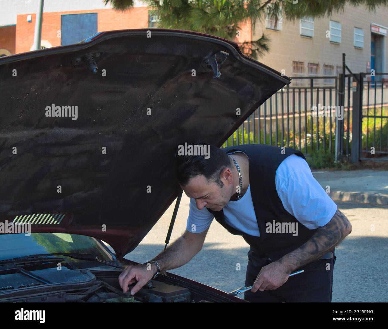 mature man repair a breakdown in his car engine with tools on the side of the road Stock Photo