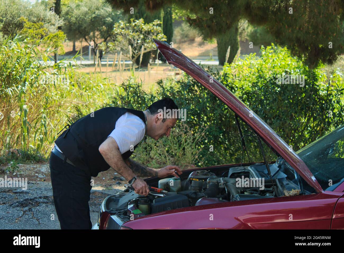 mature man fixing a breakdown in his car engine with tools on the side of the road Stock Photo