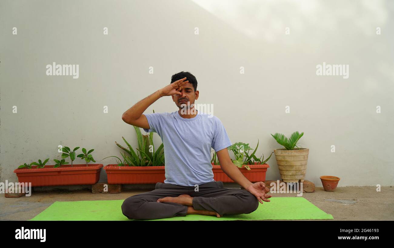 Serene Indian guy practicing yoga outdoors. Young yoga practitioner working out and sitting in lotus pose with closed eyes. Yoga and meditation concep Stock Photo