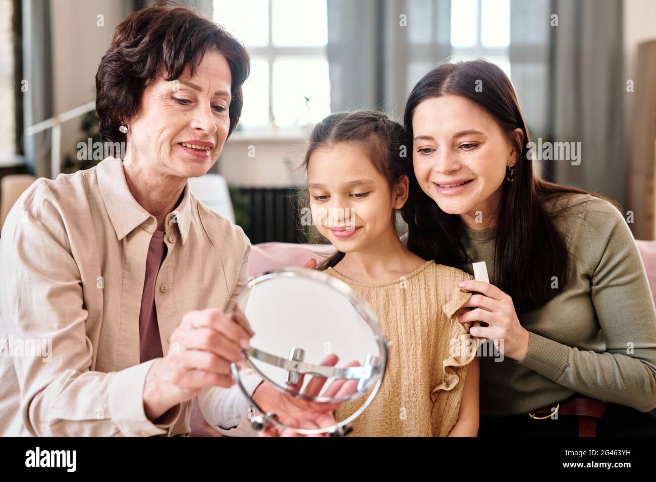 Two women and cute little girl looking in mirror while applying makeup Stock Photo