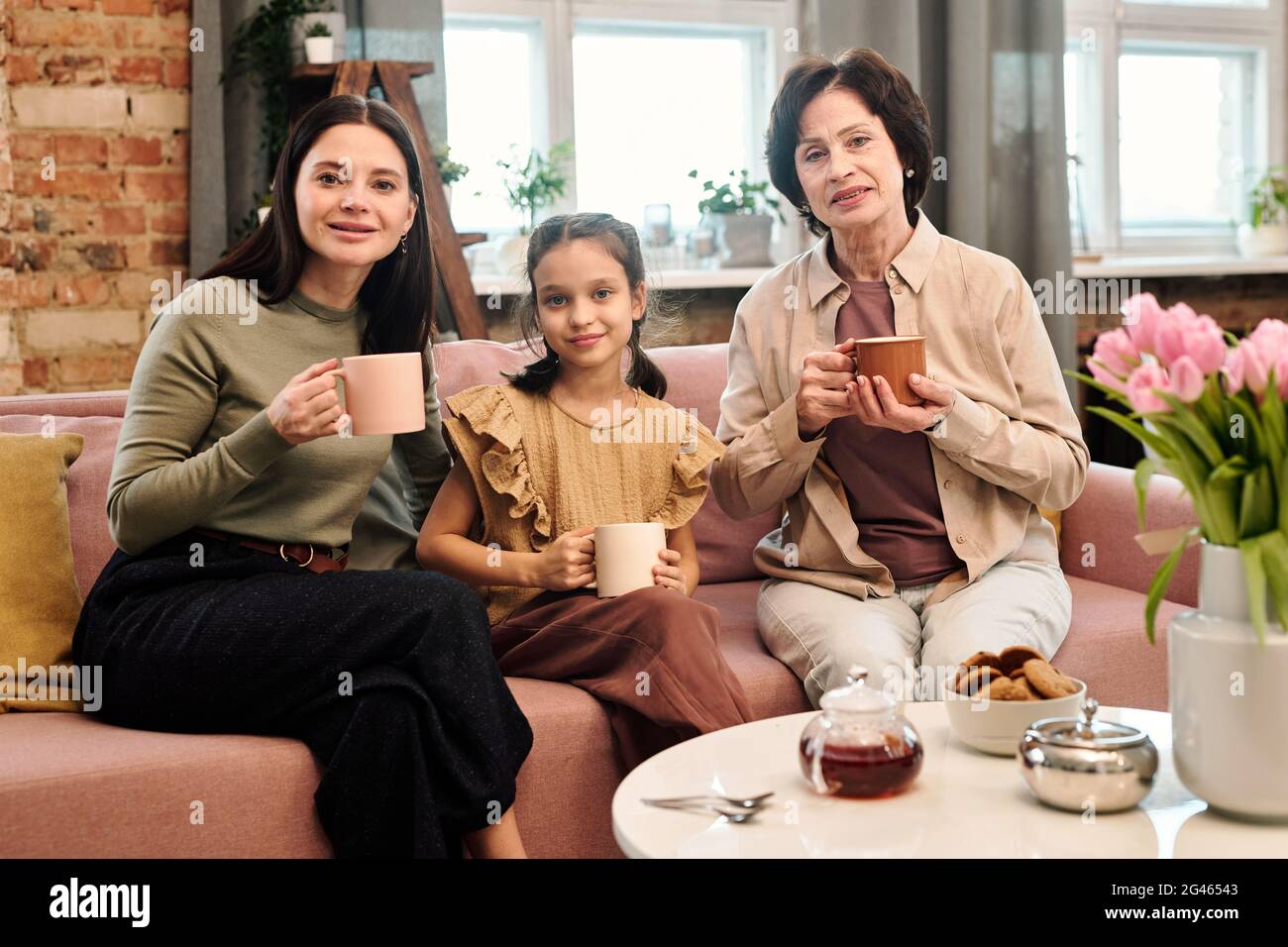 Three happy females having tea while sitting on couch by served table Stock Photo