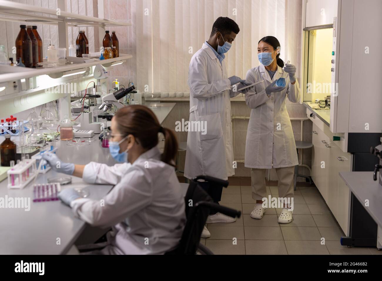 Intercultural chemists in labcoats working with new liquid substances together Stock Photo