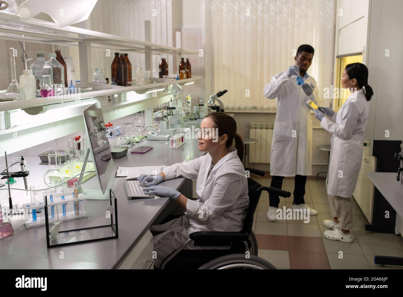 Group of intercultural scientists in whitecoats and gloves working in laboratory Stock Photo