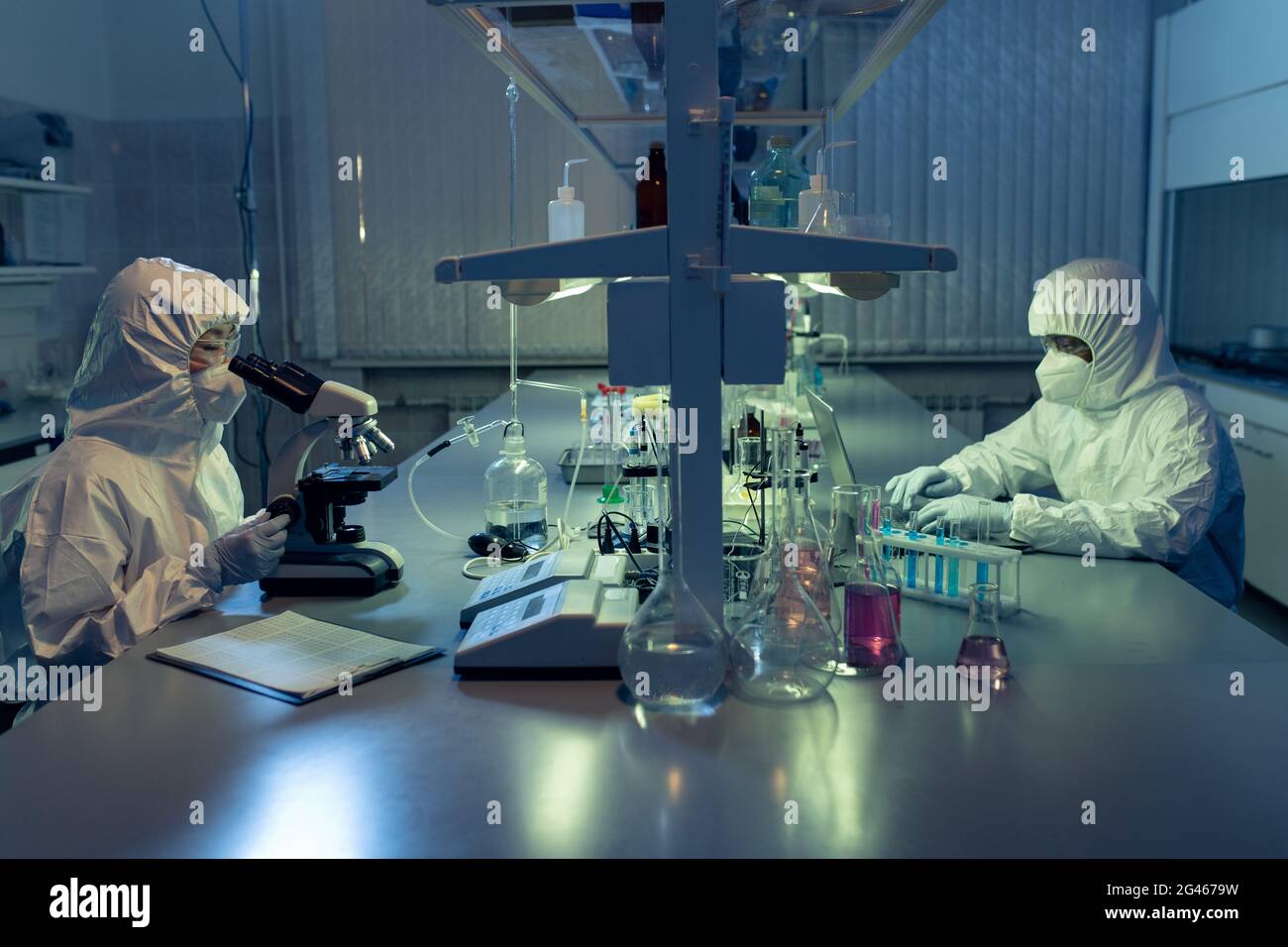 Two contemporary lab workers in coveralls using microscope and laptop Stock Photo