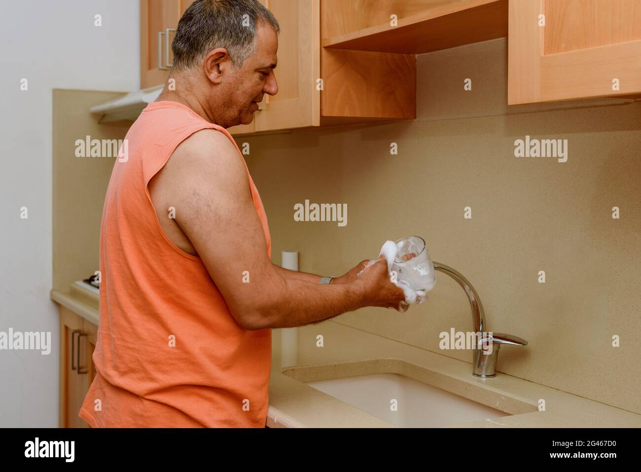 Senior man washing drinking glass in the kitchen. A mature man standing at his kitchen sink at home and washing dishes after dinner. Stock Photo