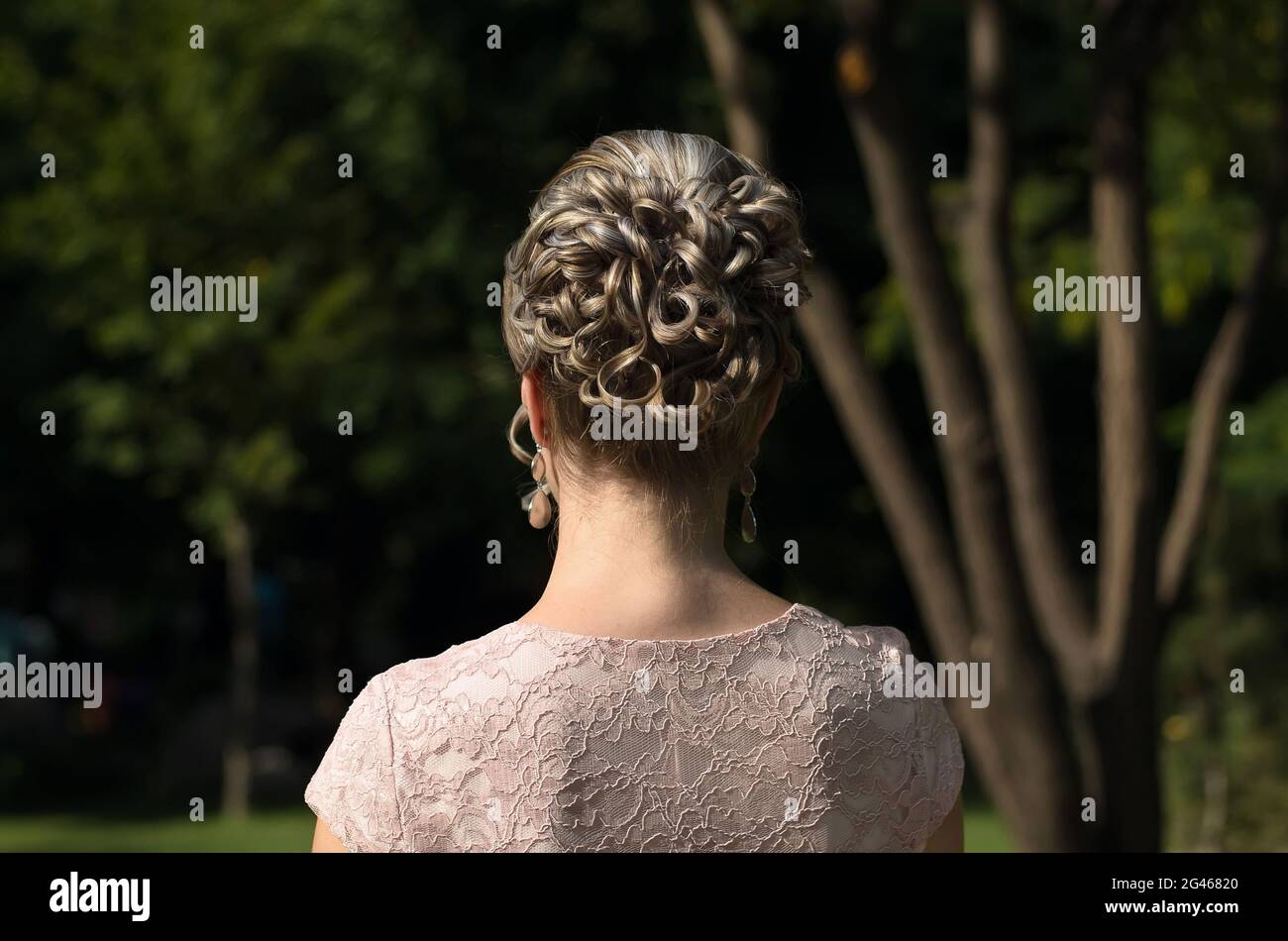 Girl from the back close-up with a beautiful hairstyle on her head, among the green trees Stock Photo