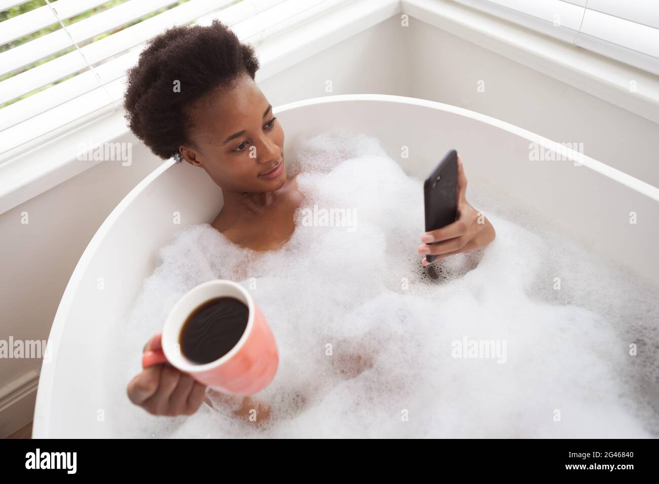 Woman with coffee cup using smartphone in a bathtub Stock Photo
