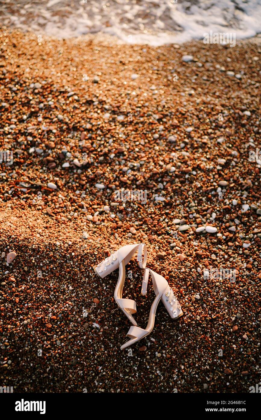 Bridal sandals with thick heels decorated with stones on a pebble beach on the sea. Stock Photo
