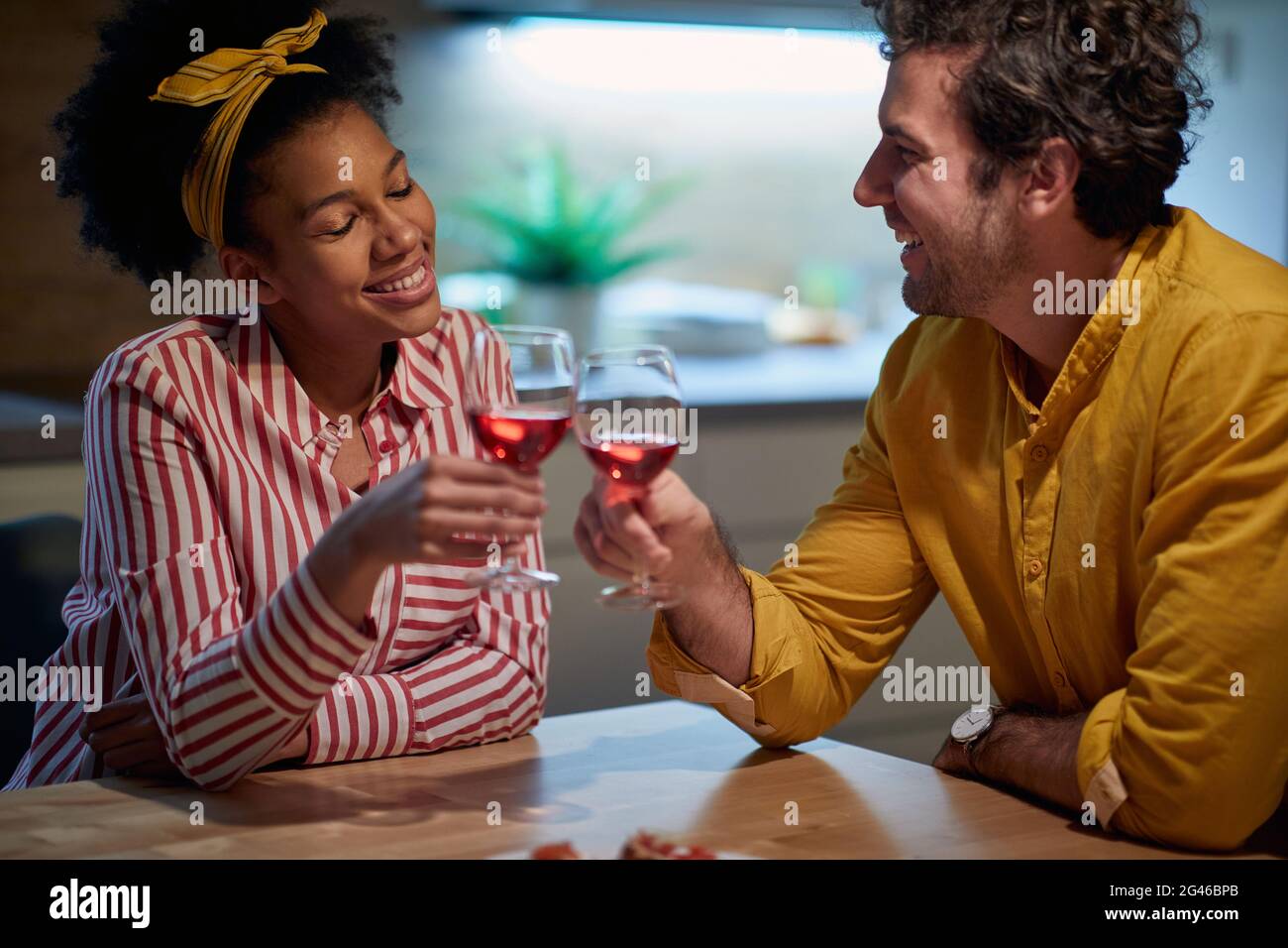 beautiful young afro-american woman pleasantly smiling while toasting with caucasian beardy man. Stock Photo