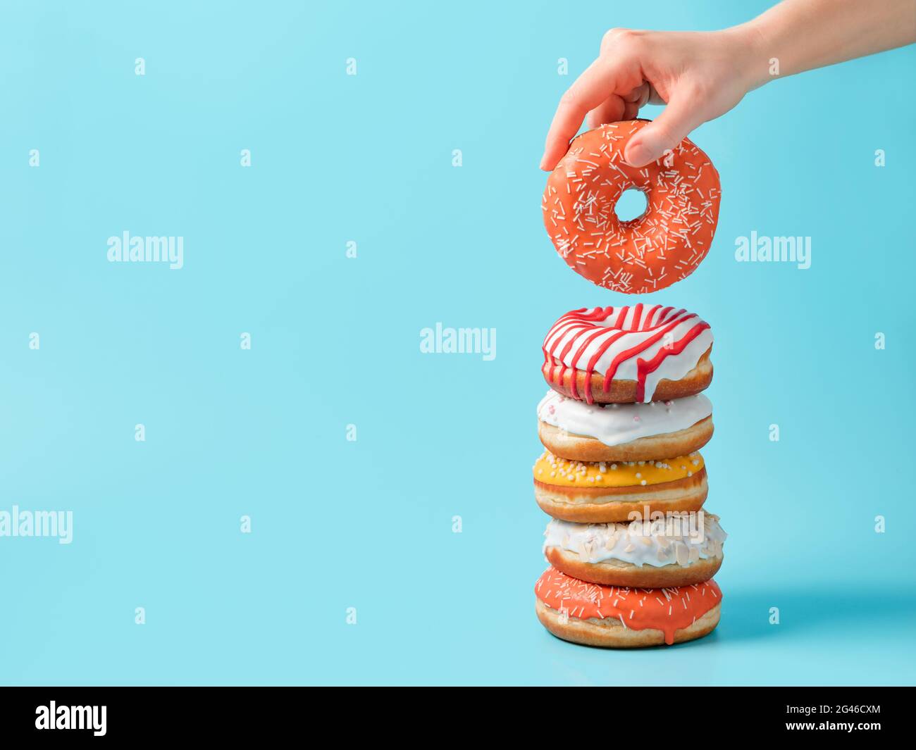 Stack of donuts, donut in hand on blue, copy space Stock Photo