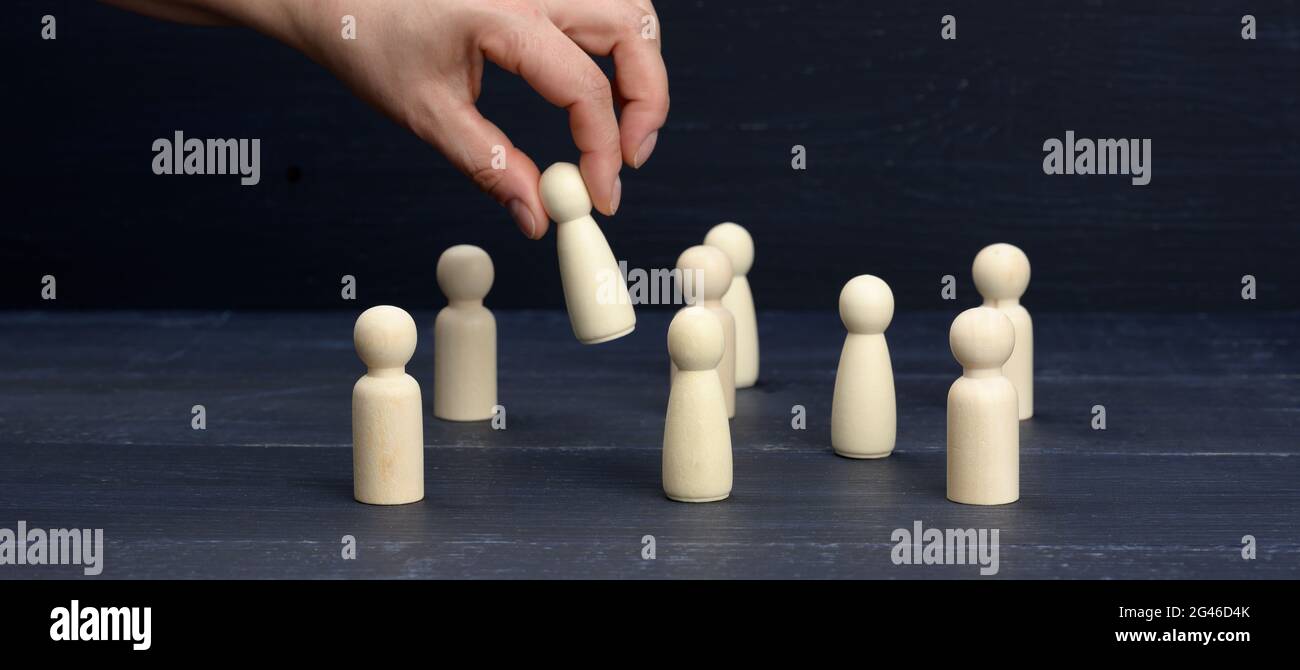 Female hand holds a wooden figurine above the crowd. The concept of finding employees, talented and unique employees Stock Photo