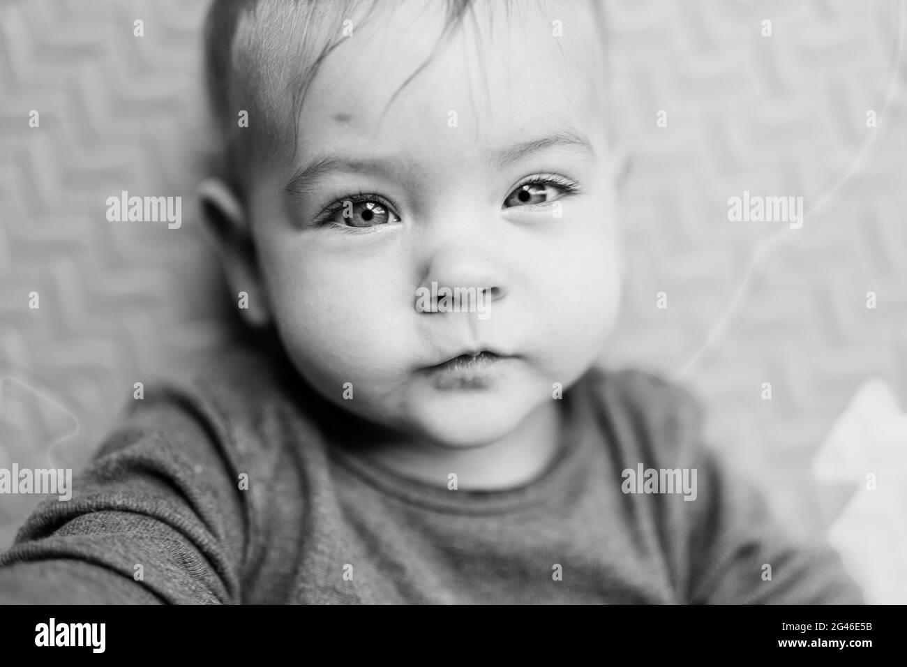 Tiny baby in a white bodysuit is lying on a rug. Portrait. Close-up. Black and white photo Stock Photo