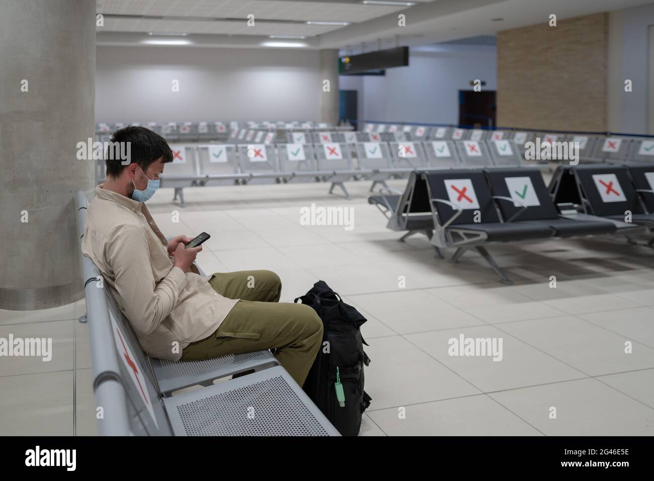 Waiting for flight at empty airport in Cyprus. Man sitting on chair with social distance marker at empty Paphos terminal. Flight Stock Photo