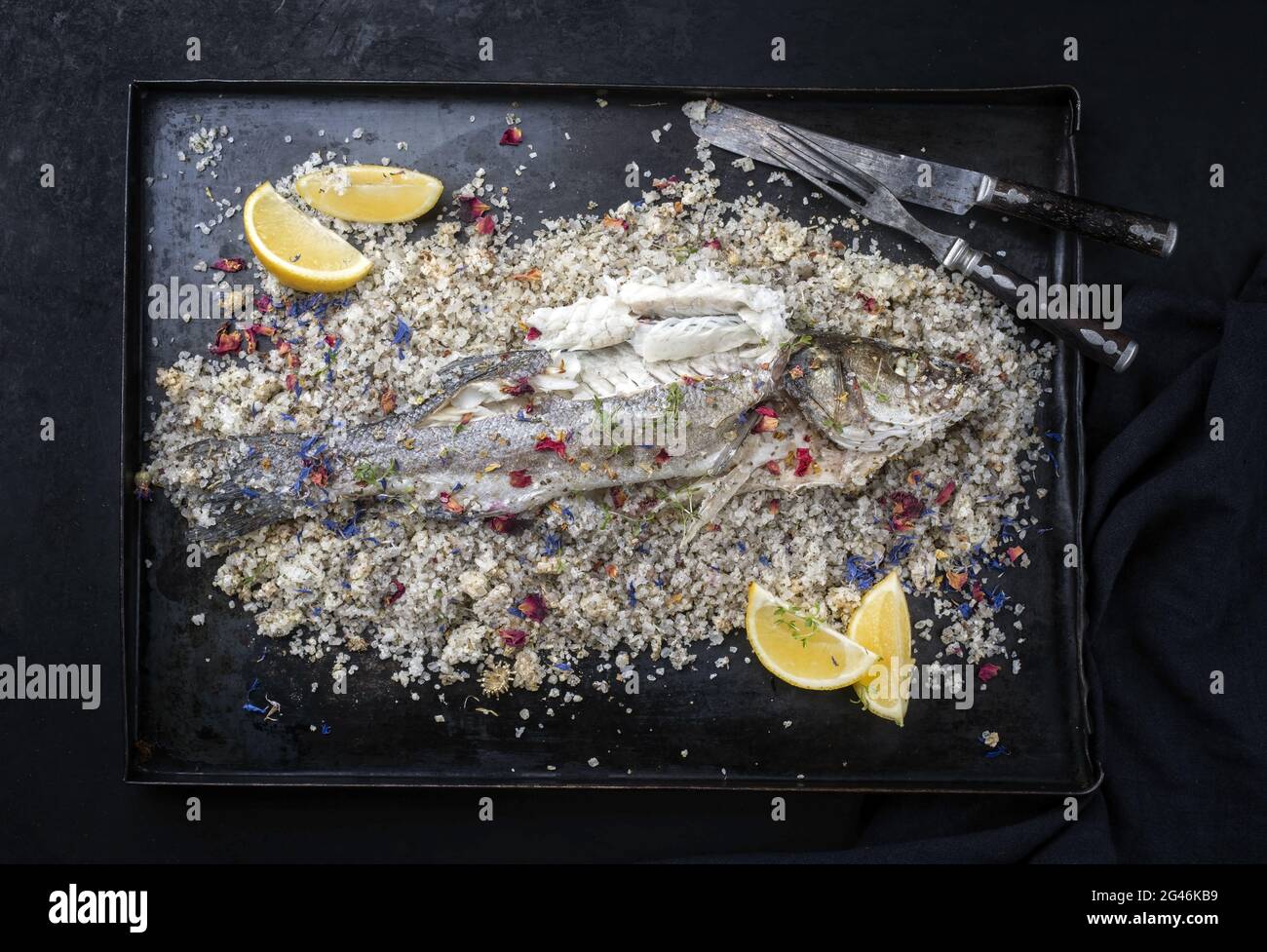 Traditional Atlantic Loup de Mer bedded into sea salt served with lemon slices and spices as top view on a rustic metal tray Stock Photo