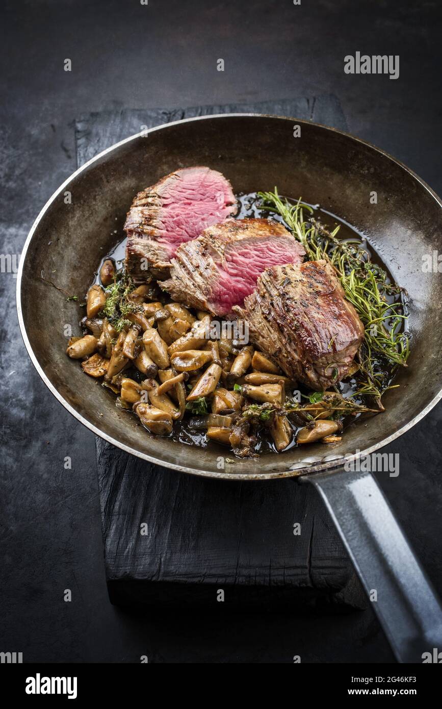 Fried dry aged beef fillet steak natural with king trumpet mushroom and herbs offered as close-up in a rustic frying pan Stock Photo