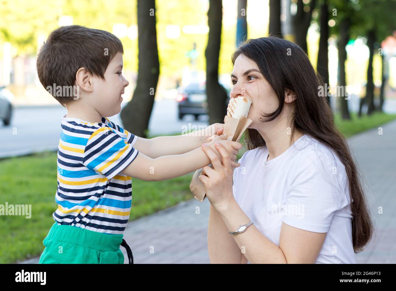 A baby boy feeds his mother a shaurma in the street. Advertising fast food and street food. Stock Photo