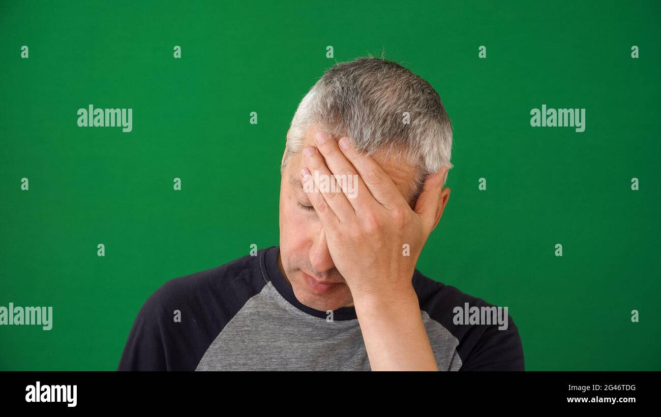 Fatigue in the human face. A mature adult man of European descent with gray hair on the green screen background. Portrait of a male with signs of depl Stock Photo