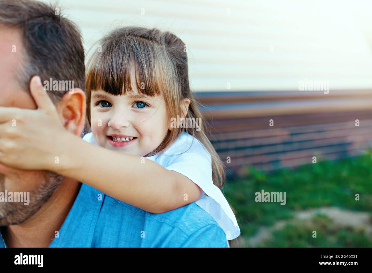 Happy little girl hugs dad on the street. The child plays blind man's buff with the parent. Stock Photo