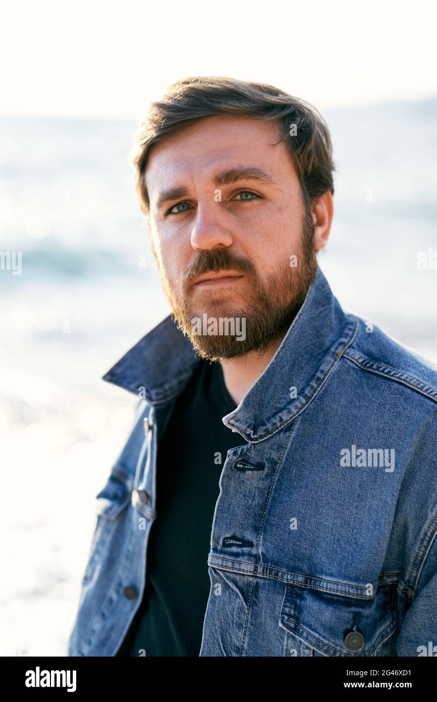 Portrait of a pensive man in a denim jacket against the background of the sea. Close-up Stock Photo