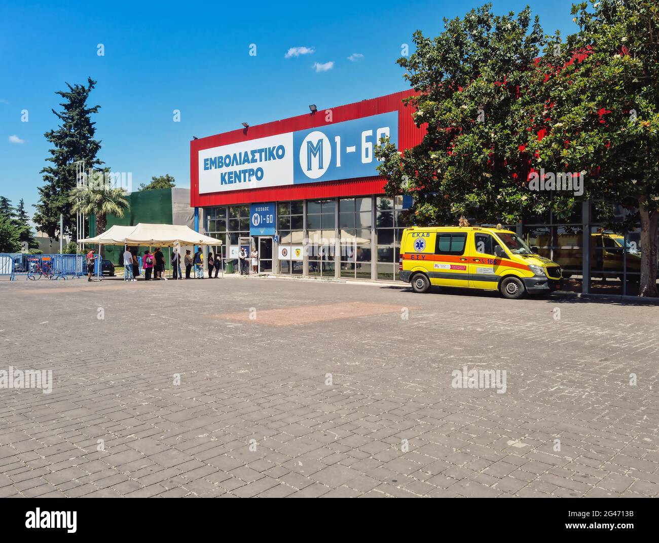 Thessaloniki, Greece - June 15 2021: Mega covid-19 vaccination center entrance with sign in Greek. Crowd outside converted Helexpo International Fair premises where daily inoculations are conducted. Stock Photo