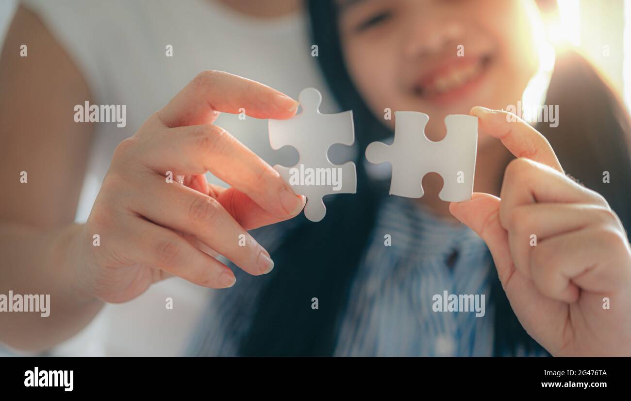 Happy family, Asian daughter playing jigsaw puzzle with her mother for