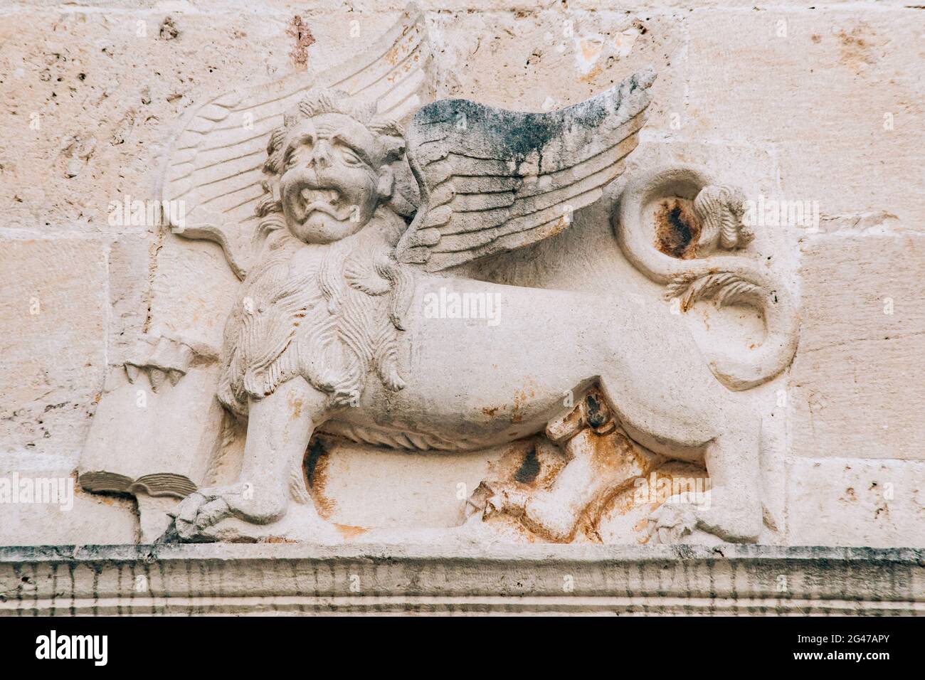 A bas-relief on the wall depicting a mythical lion with wings and a book in its paws. Stock Photo