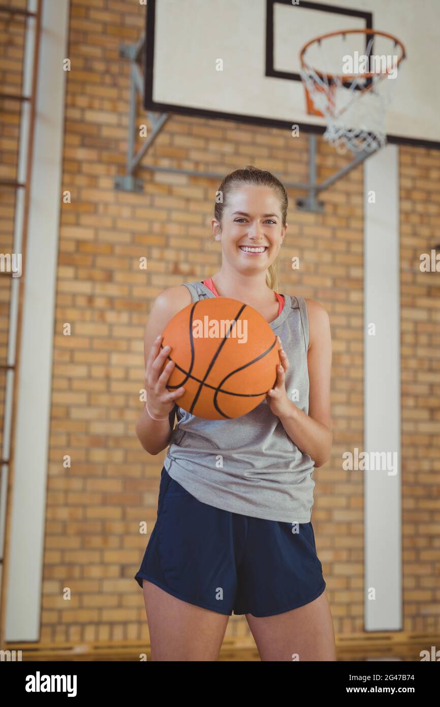 Smiling high school girl holding a basket ball in the court Stock Photo