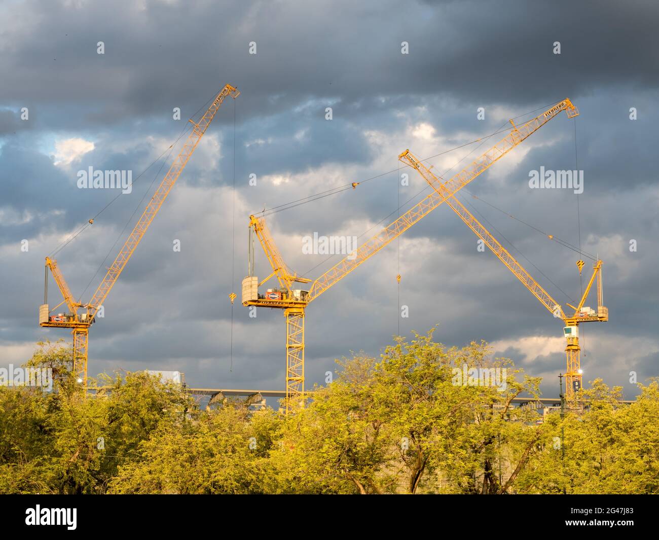 Construction cranes working under cloudy evening sky Stock Photo - Alamy