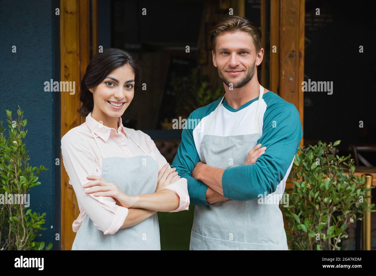 Portrait of smiling waiter and waitress standing with arms crossed ...