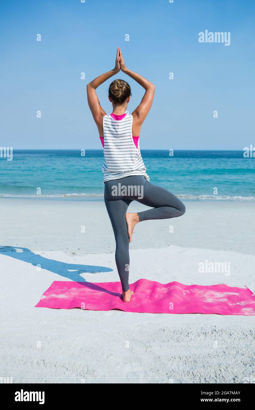 Rear view of woman practicing yoga in tree pose at beach Stock Photo ...