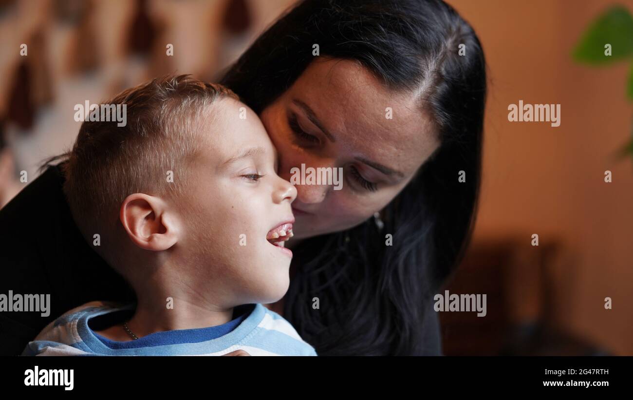 Close up portrait of a little boy with special needs and mom laughing at a table in a cafe, lifestyle. Mom's love for her child, inclusion.Happy disab Stock Photo