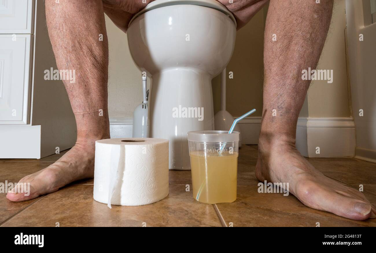 Close up of legs of senior caucasian adult sitting on toilet preparing for colonoscopy with medication Stock Photo