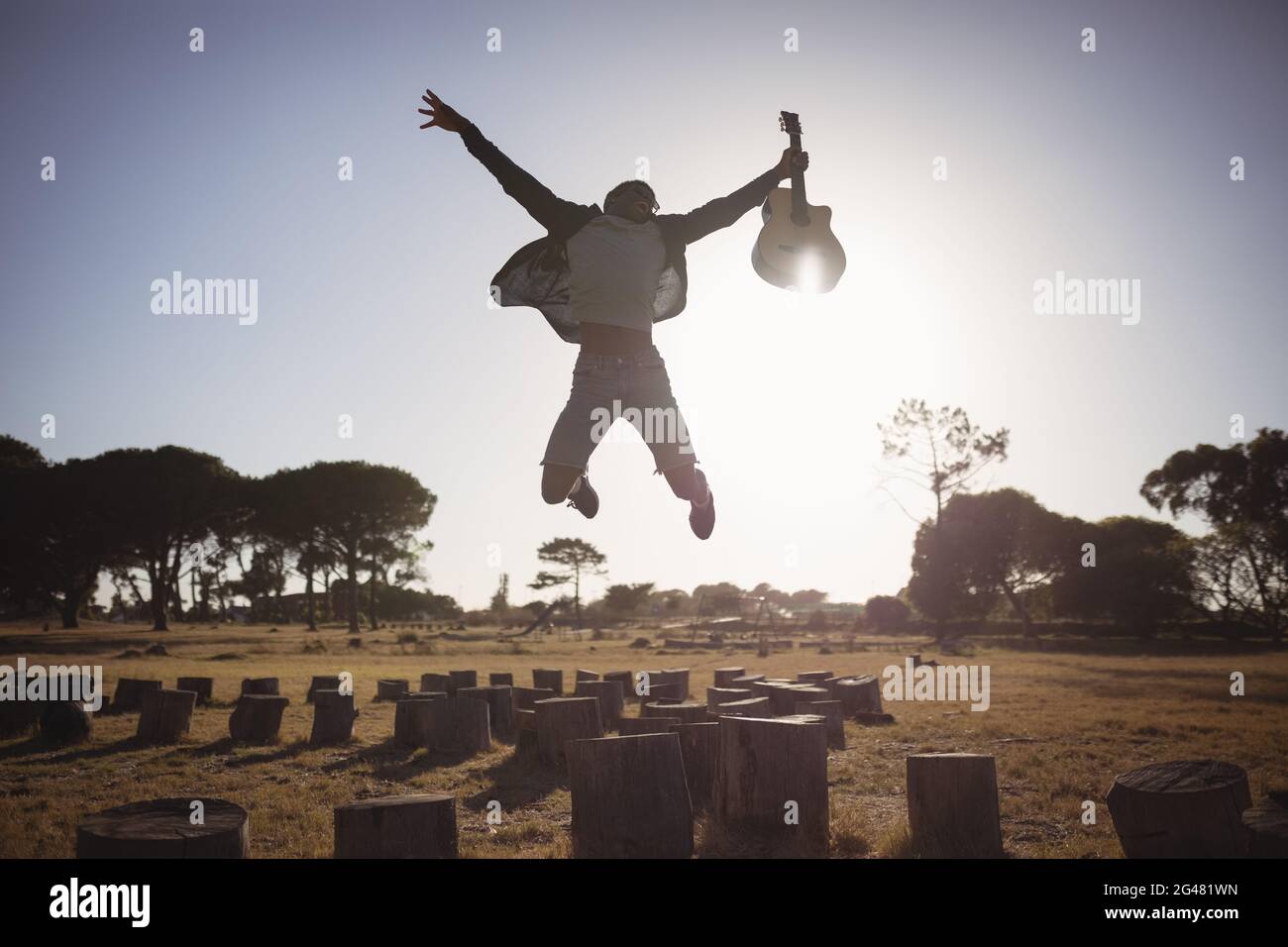 Happy man holding guitar while jumping against clear sky Stock Photo