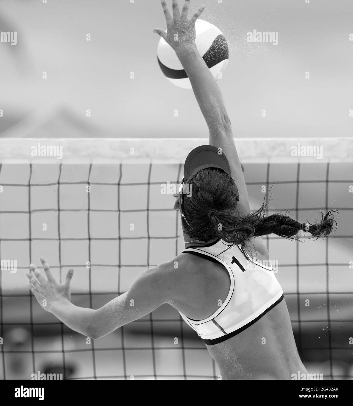 A Beach Volleyball Player Is Jumping At The Net And Spiking The Ball Down In Vertical Black And White Image Format Stock Photo