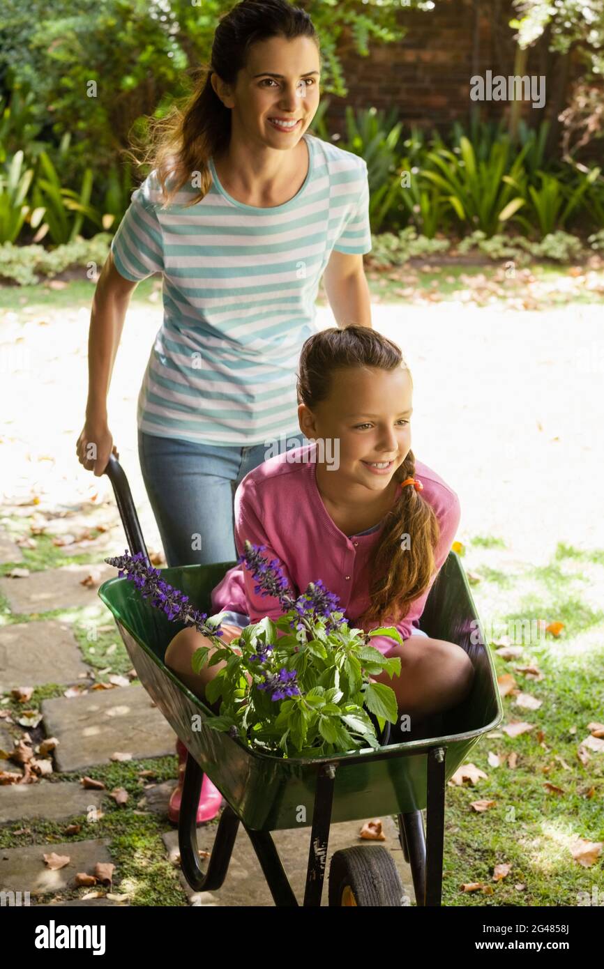 Smiling mother pushing girl with flowers sitting in wheelbarrow Stock ...