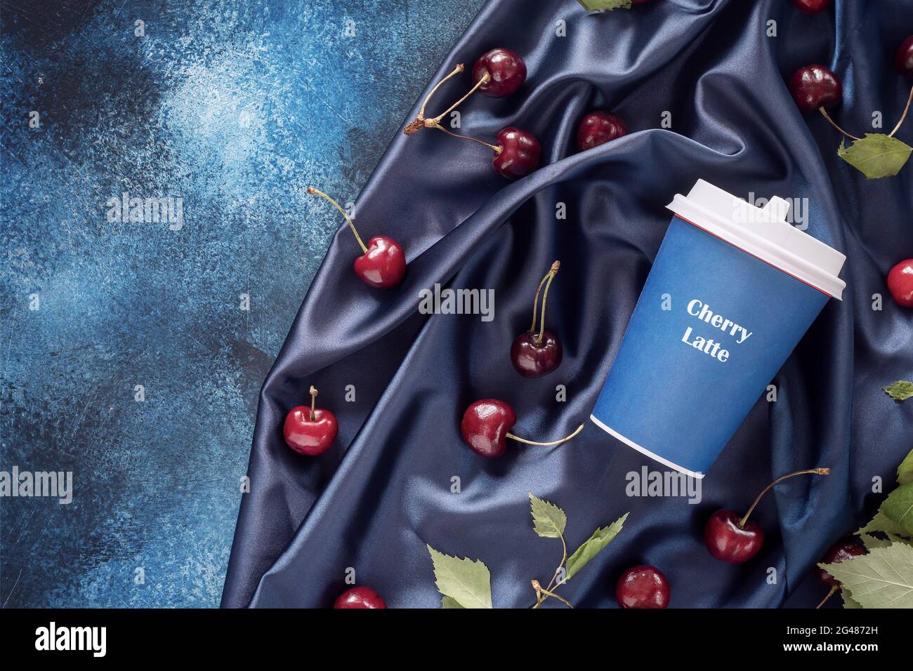 Food composition with craft cup of coffee, cherries and leaves on a blue, satin, folded background with copy space. Cherry latte, new kind of coffee Stock Photo