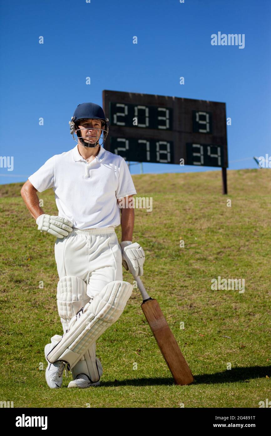 Confident cricket player with bat standing against scoreboard Stock