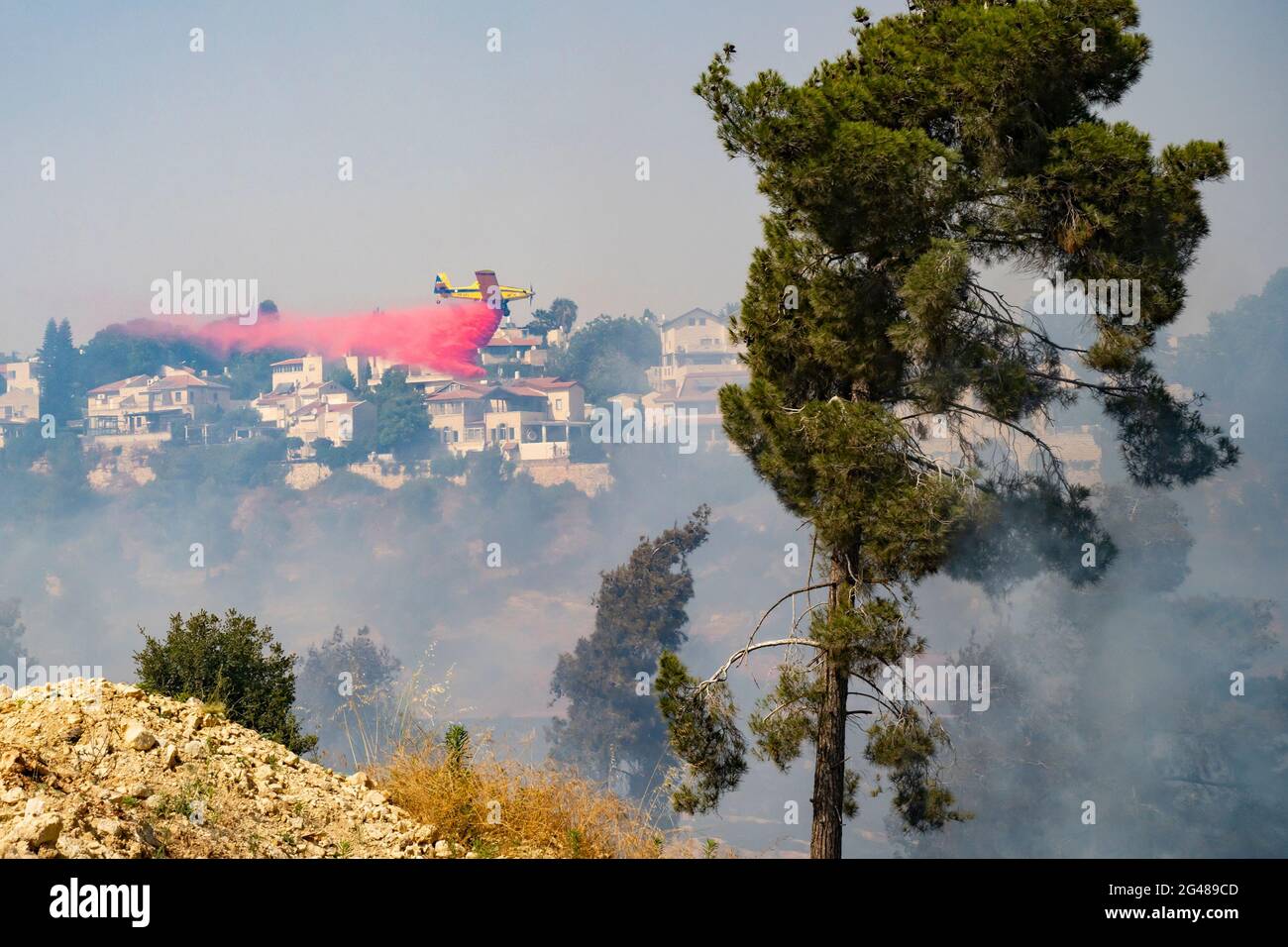 Mevasseret Zion, Israel - June 19th, 2021: A firefighter airplane drops flame retardant over a pine forest fire on the municipal border of a town near Stock Photo