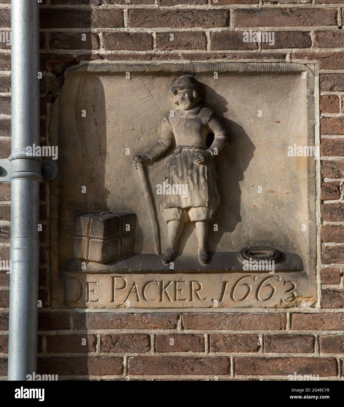 Facing brick with standing man with package and rope and inscription: the Packer 1663. A sandstone facing brick on which: the pinker 1663, and a standing man with a suit and a rope beside him. Stock Photo