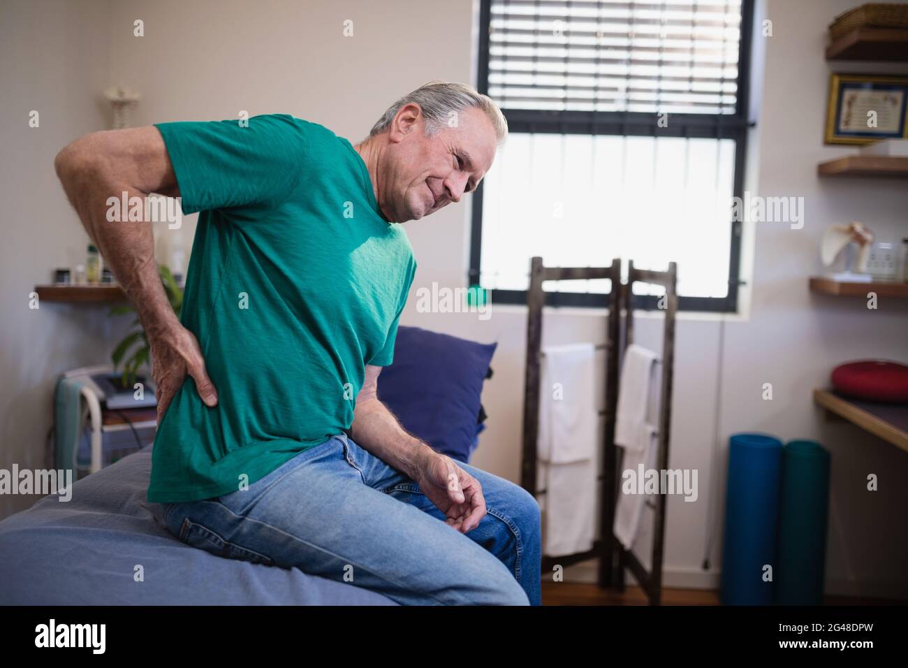 Side view of male patient suffering from back ache while sitting on bed