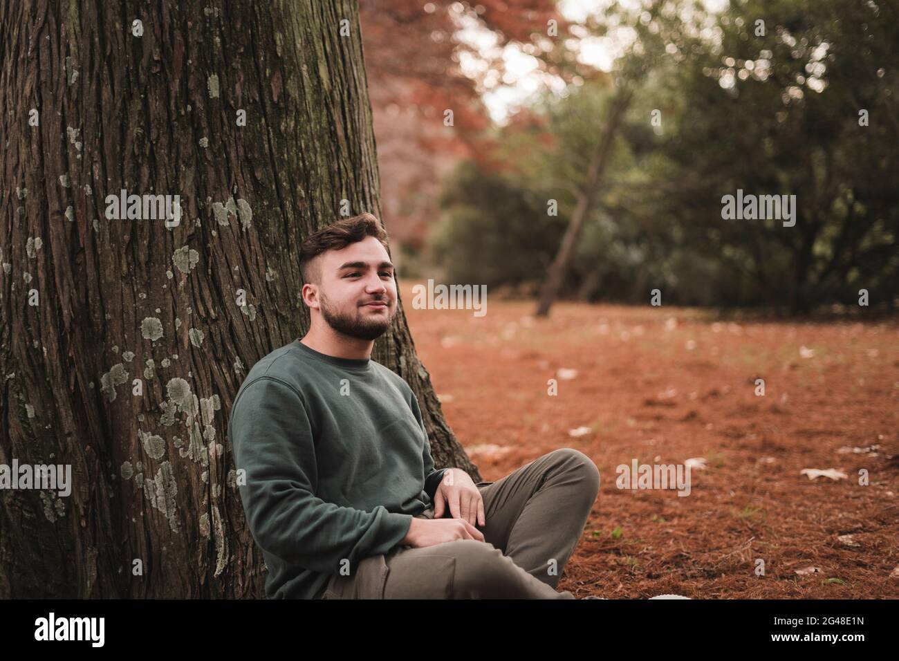 Young man sitting next to a tree in a park Stock Photo