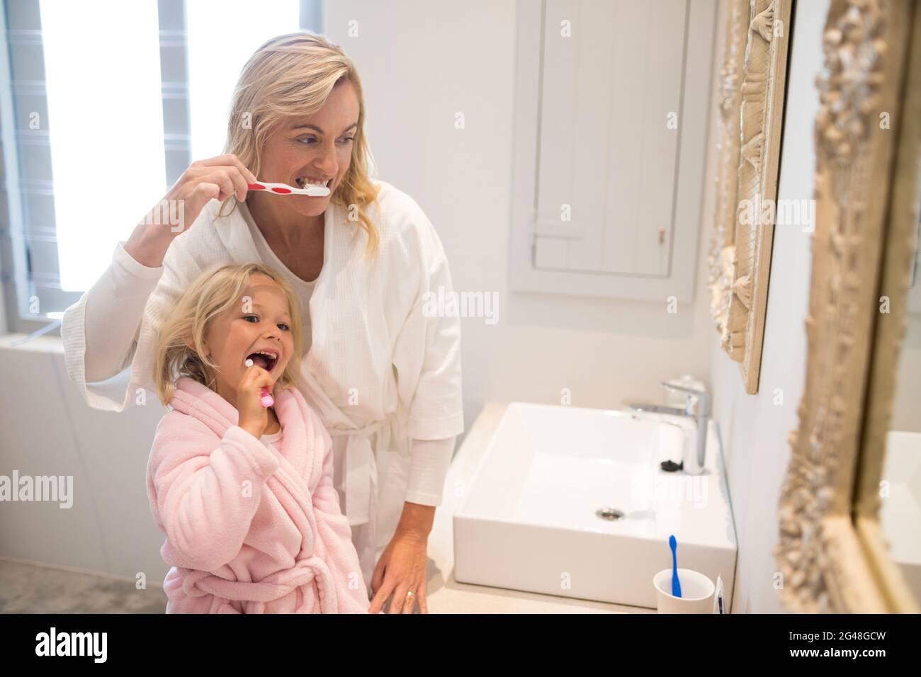 Mother and daughter brushing teeth in bathroom Stock Photo