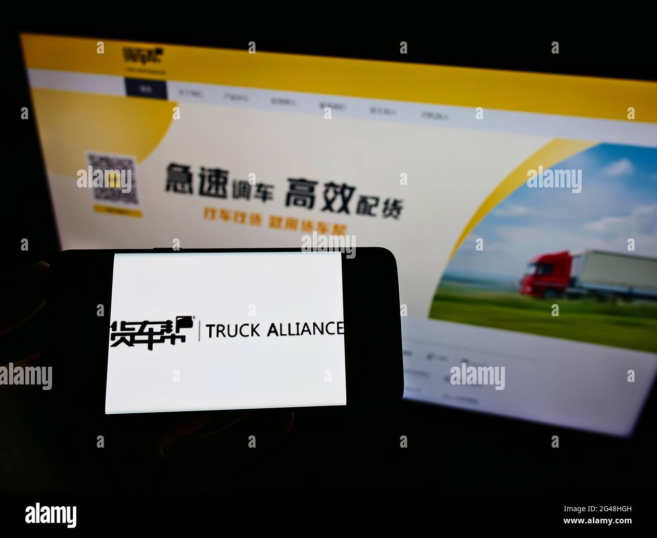 Person holding cellphone with logo of Chinese logistics platform company Truck Alliance on screen in front of webpage. Focus on phone display. Stock Photo