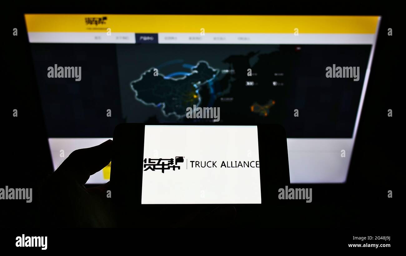 Person holding smartphone with logo of Chinese logistics platform company Truck Alliance on screen in front of website. Focus on phone display. Stock Photo
